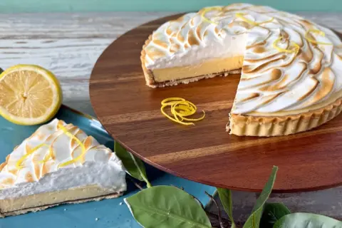 Ein köstliches Zitronentarte Rezept: Ganze Tarte und ein Stück mit Baiserhaube, garniert mit Zitronenzesten.