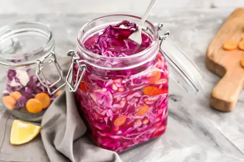 Roter Kohl und Karotten in Gläsern, bereit zum Kohl haltbar machen. Ein Löffel ragt aus dem vorderen Glas.