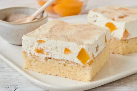 Saftiger Pfirsich Schmand Kuchen mit Zimt bestreut, serviert auf einem weißen Teller.