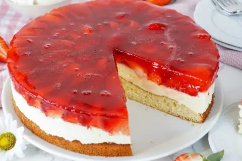 Ein saftiger Erdbeerkuchen mit Vanillepudding und einer glänzenden Erdbeer-Gelee-Schicht. Ein Stück ist bereits herausgeschnitten.
