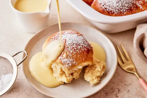 Ein Buchtel wird mit Vanillesauce übergossen, bestäubt mit Puderzucker. Ein köstliches Buchteln Rezept zum Genießen.