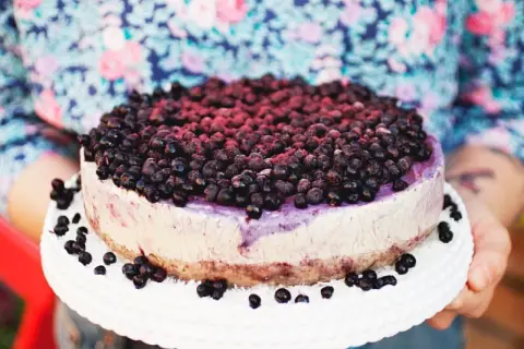 Ein köstlicher Blueberry Cheesecake, üppig belegt mit frischen Blaubeeren, wird auf einem weißen Tortenständer präsentiert.