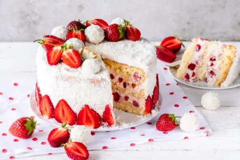 Eine köstliche Erdbeer Raffaello Torte, umhüllt von Kokosraspeln und dekoriert mit frischen Erdbeeren und Raffaello Kugeln.