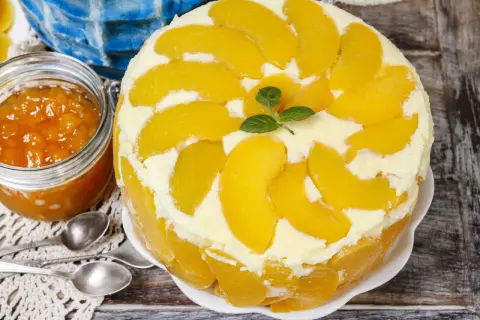 Eine köstliche Pfirsich Maracuja Torte, dekoriert mit frischen Pfirsichspalten und Minze. Daneben ein Glas Pfirsichmarmelade.