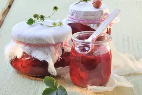 Gläser mit selbstgemachtem Erdbeerkompott, bereit zum Einkochen. Ein Holzlöffel steckt in einem Glas.