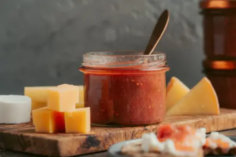 Glas mit rotem Chutney, daneben Käsewürfel und -stücke. Perfekt für leckere Chutneys Rezepte.