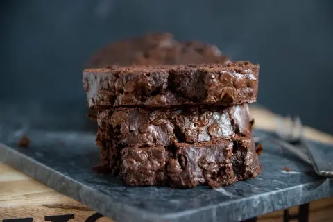 Ein saftiges Bananenbrot mit Schokolade, in Scheiben gestapelt, auf einem dunklen Stein serviert.