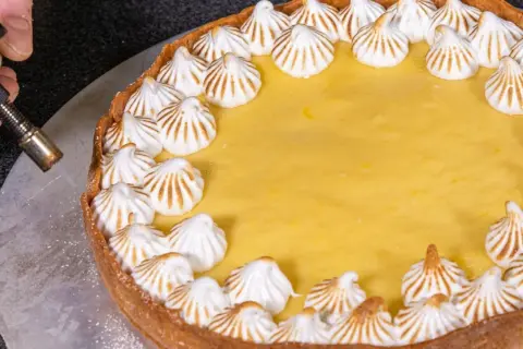 Ein köstlicher Lemon Curd Kuchen mit Baiserhauben wird mit einem Brenner karamellisiert.