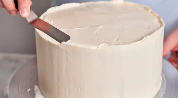 Eine Hand glättet mit einem Spatel die cremige Buttercreme-Torte.