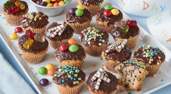 Bunte Muffins mit Schokoglasur und Gummibärchen, perfekt für einen Kindergeburtstag.