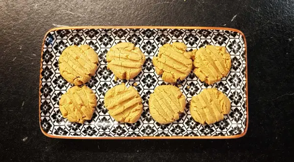 A rectangular plate with a black and white floral pattern holds eight golden-brown kekse ohne zucker.