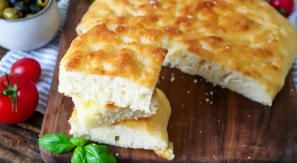 Frisch gebackenes Focaccia-Rezept, aufgeschnitten und gestapelt, mit Tomaten und Oliven daneben.