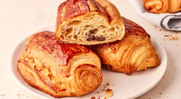 Zwei goldbraune, knusprige Pain au Chocolat auf einem Teller, eines davon angeschnitten, enthüllt die schokoladige Füllung.