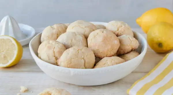 Schüssel voller zitronen cookies, daneben Zitronen und ein Zitronenpresse. Ein Cookie ist angebrochen.
