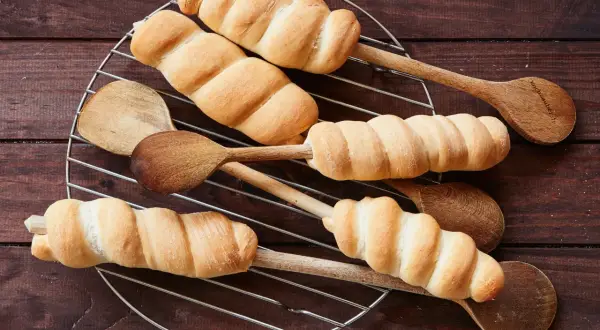 Frisch gebackenes Stockbrot mit frischer Hefe, auf Holzkochlöffeln auf einem Gitterrost arrangiert.