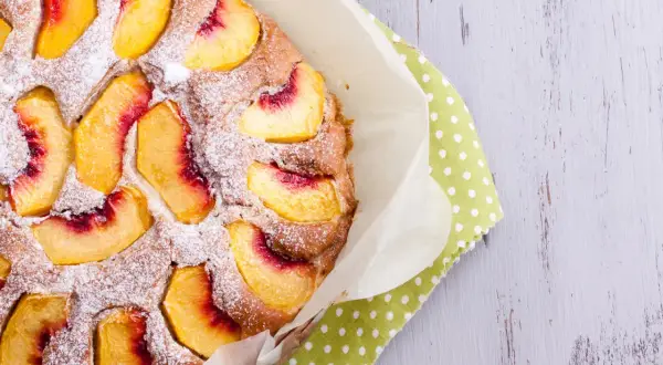 Saftiger Pfirsichkuchen, mit Puderzucker bestäubt, auf einem grünen Tupftuch. Ein Genuss für die Sinne!