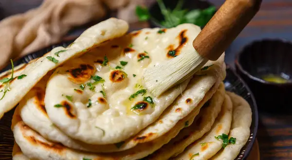Frisch gebackenes indisches Fladenbrot wird mit Butter bestrichen und mit Koriander bestreut.