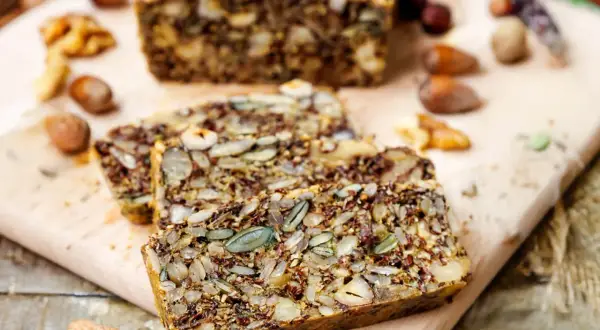Slices of hearty keto brot, packed with seeds and nuts, rest on a wooden board.