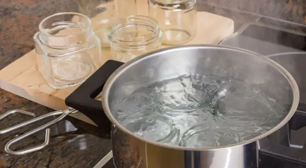 Gläser werden für das Einkochen mit Schraubdeckel sterilisiert. Ein Topf mit kochendem Wasser und ein Glasheber liegen bereit.