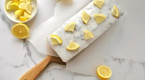 Ein köstlicher zitronen mohn kuchen, verziert mit frischen Zitronenspalten und Mohn. Daneben eine Schale mit Zitronenstücken und ganze Zitronen.