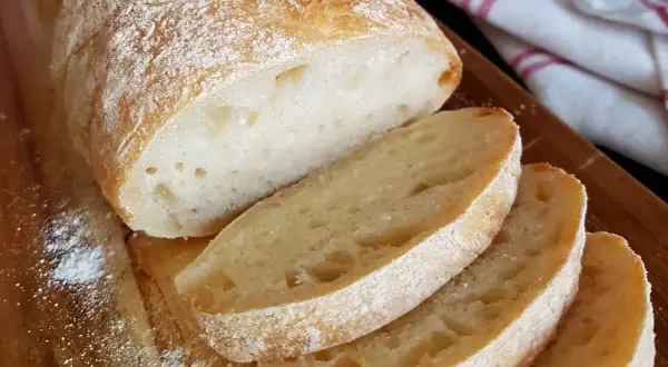 Frisch gebackenes ciabatta brot mit knuspriger Kruste und luftiger Krume, auf einem Holzbrett mit etwas Mehl bestäubt.
