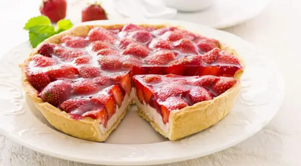 Ein saftiger Erdbeerkuchen mit Quarkfüllung, bedeckt mit frischen Erdbeeren und glänzendem Tortenguss. Ein Stück ist bereits entnommen.