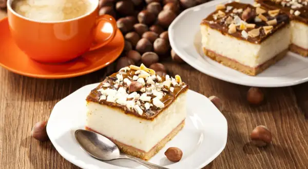 Ein Stück cremiger Käsekuchen mit Schokoladenglasur und Nüssen, dazu eine Tasse Kaffee. Perfekt für einen schnellen Kuchengenuss.