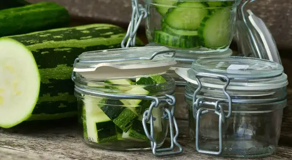 Zucchini-Scheiben und -Würfel in Gläsern, bereit zum einkochen im Dampfgarer. Frische Zucchini liegt daneben.