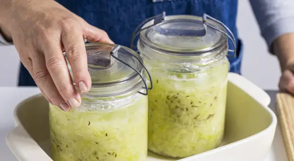 Hände setzen zwei Gläser mit Sauerkraut zum Fermentieren in ein Gefäß.