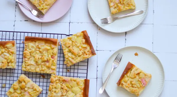 Saftiger Rhabarberkuchen auf Hefeteig mit Streuseln, auf Tellern und einem Kuchengitter arrangiert.