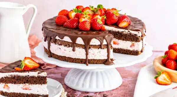 Schokoladenkuchen mit Erdbeercreme, Schokoladenglasur und frischen Erdbeeren, ein Stück angeschnitten.
