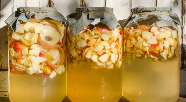 Drei Gläser mit Apfelschnitzen und Flüssigkeit, bereit, um Apfelessig selber zu machen.