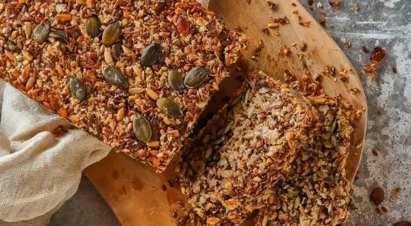 Brot ohne Mehl, reich an Saaten wie Kürbis- und Leinsamen, liegt auf einem Holzbrett.