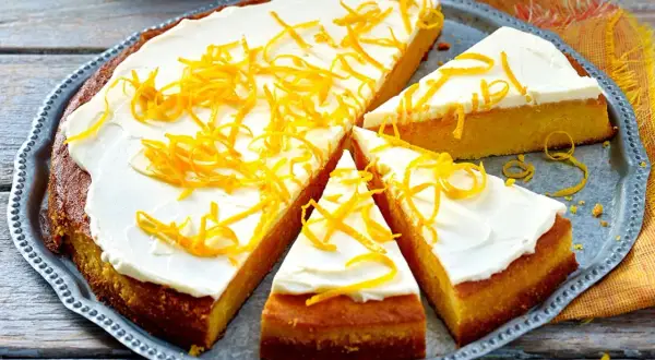 Ein saftiger, gesunder Kuchen mit weißem Zuckerguss und orangen Zesten verziert, auf einem silbernen Blech.