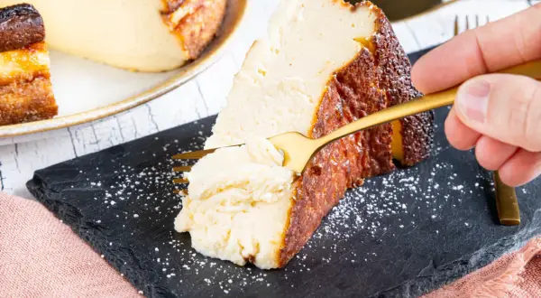 Ein Stück cremiger San Sebastian Cheesecake wird mit einer goldenen Gabel probiert.