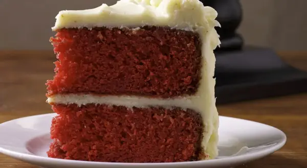 Ein Stück saftiger **red velvet** Kuchen mit cremiger Glasur auf einem weißen Teller.
