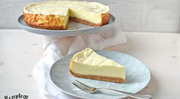 Ein cremiger american cheesecake mit Keksboden, ein Stück auf einem Teller mit Gabel.