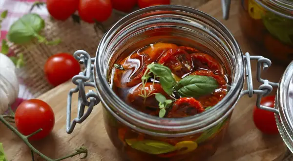 Eingeweckte Tomaten in Öl, garniert mit Basilikum. Die Haltbarkeit von Eingewecktem ist oft lang, wenn richtig gelagert.