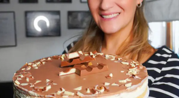 Lächelnde Frau präsentiert eine köstliche Kinderriegel Torte, dekoriert mit Schokostückchen und ganzen Riegeln.