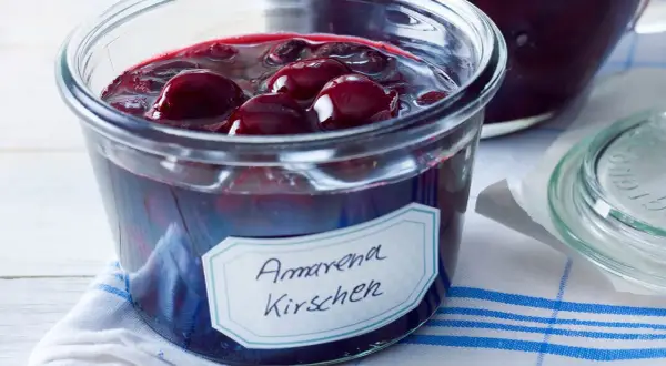 Ein Glas mit Amarena Kirschen, perfekt für ein Amarena Kirschen Rezept. Die dunklen Früchte schwimmen in Sirup.