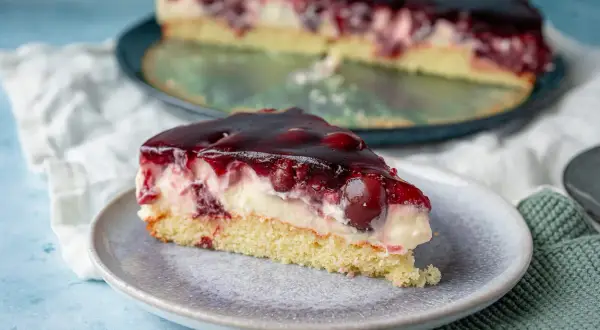 Ein saftiges Stück Kirsch Schmand Kuchen mit Kirschen und einer glänzenden Geleeschicht auf einem Teller.