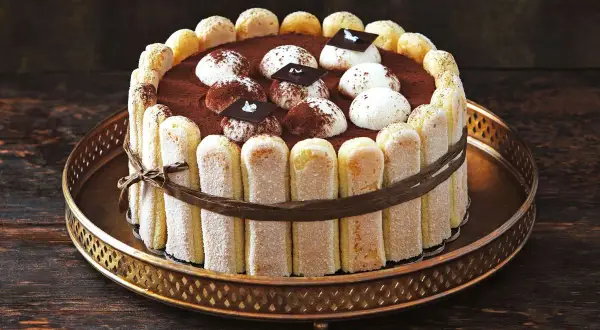 Eine köstliche Tiramisu Torte, umrandet von Löffelbiskuits und verziert mit Kakao und Schokoladenstückchen.