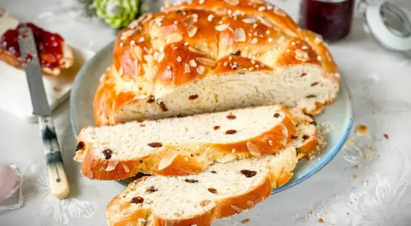 Ein goldbraunes Osterbrot mit Rosinen und Mandelsplittern, perfekt gebacken mit Trockenhefe. Dazu ein Glas Marmelade.