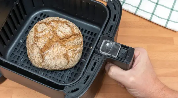 Ein goldbraunes Brot liegt im Korb eines Airfryers. Perfekt für schnelles brot backen im airfryer.