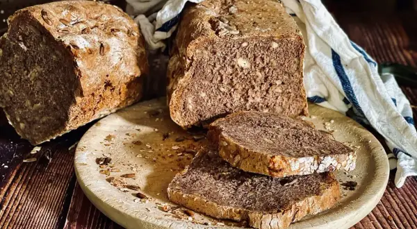 Frisch gebackenes Dinkelbrot mit Körnern und Nüssen, auf einem Holzbrett mit zwei Scheiben.