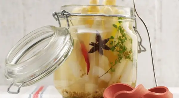 Ein Glas mit eingelegtem Spargel, Gewürzen und Kräutern. Der Deckel ist geöffnet.