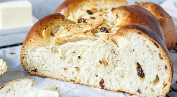 Ein goldbrauner Hefezopf mit Rosinen, frisch gebacken und bereit zum Genießen. Daneben liegt ein Stück Butter.