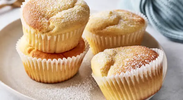Saftige Muffins mit Quark, bestäubt mit Puderzucker, auf einem Teller arrangiert.