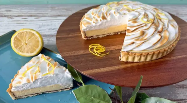 Ein köstliches Zitronentarte Rezept: Ganze Tarte und ein Stück mit Baiserhaube, garniert mit Zitronenzesten.