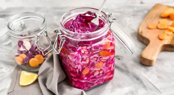 Roter Kohl und Karotten in Gläsern, bereit zum Kohl haltbar machen. Ein Löffel ragt aus dem vorderen Glas.